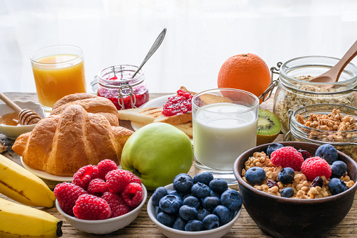 Healthy breakfast buffet with various morning food and drinks. Oats, granola, croissant, milk, oatmeal, toast, fruit, berries, nuts, orange juice. Assortment of tasty vegetarian food.