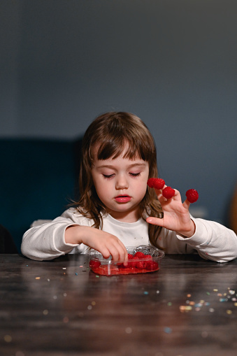 Little girl eating raspberries at home.