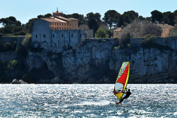 Optimist boats, with Le Lavandou town in background. Four small sailing vessels in single file, navigate behind each other. Le Lavandou, in Var in France. April 16, 2015