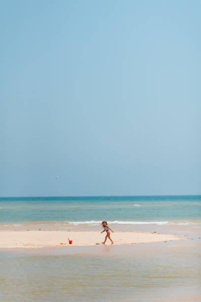 Funny slender cheerful girl playing with small waves, kicking their feet and spinning in place under the warm bright summer sun enjoying the long-awaited vacation