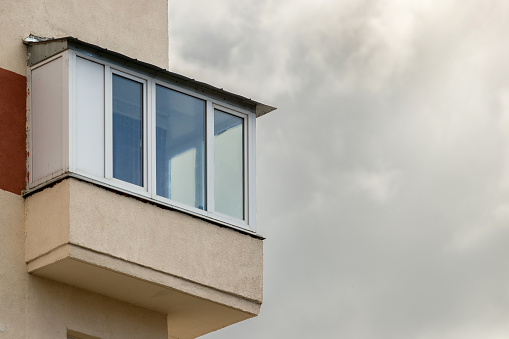 Glazed balcony of an apartment building against a cloudy sky.