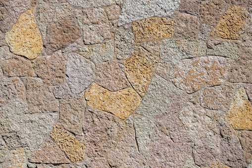 Textured wall of multicolored natural stone in a random layout.