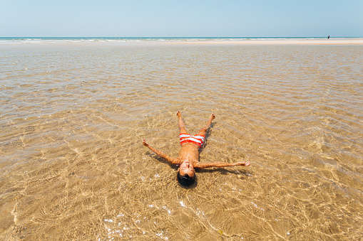 Boy lying in the shallow water and enjoys the sun, sunbathing on his summer vacation in the Algarve region in Portugal