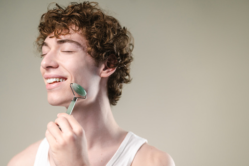 Photo of Gen Z man taking care of his skin with a face roller