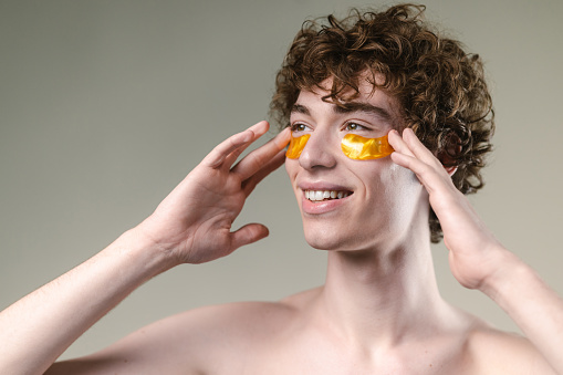 Photo of young man using under eye patches. Studio shot
