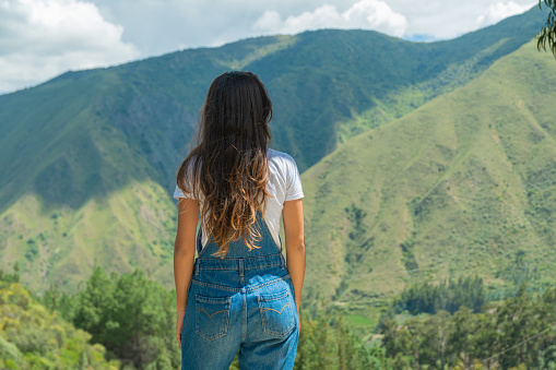 A young woman standing on the top of a mountain looking towards the horizon, enjoying her freedom, after climbing to a mountain top