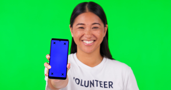 Phone, green screen and portrait of volunteer woman with charity website fund information mockup. Asian person hand with smartphone and tshirt for nonprofit contact, NGO or donation tracking markers
