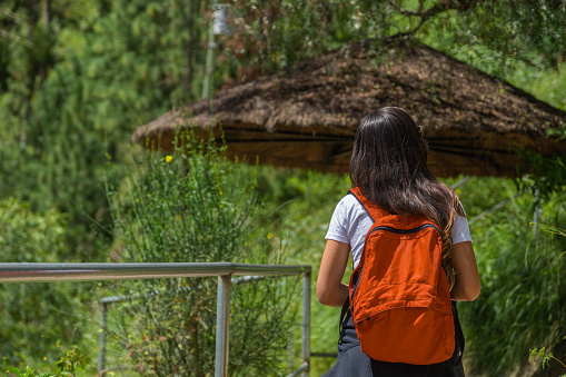A young female backpacker walking on a mountain trail, with a red backpack on her back, enjoying fresh air and outdoor scenery