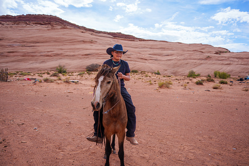Handsome Young Fourteen Year Old Navajo Boy Wearing Cowboy Hat Riding His Horse Bareback on a Ranch in Monument Valley Arizona