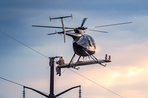 Helicopter hovering in flight with mechanic sitting on the outside fixing power lines repairing wires.