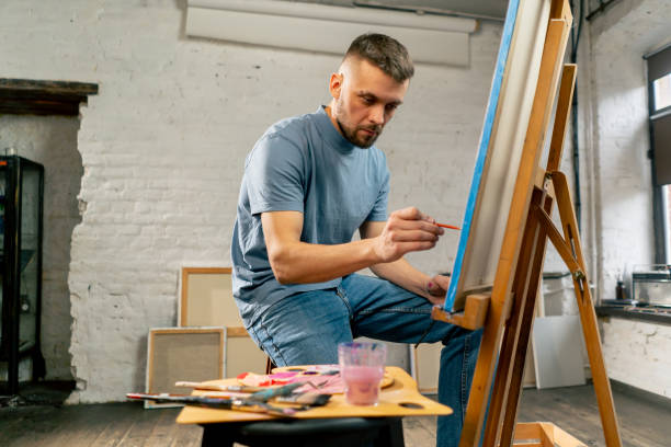 young artist in a blue t-shirt in an art studio working on painting while sitting