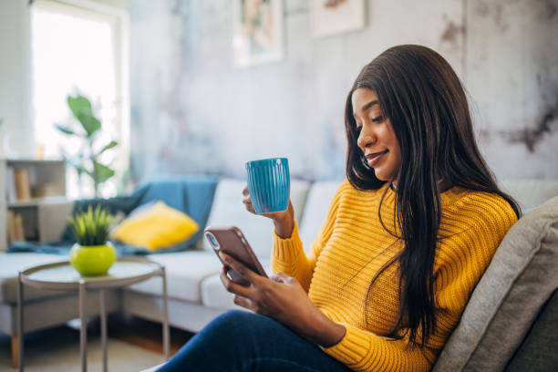 istock Woman on couch with cup looking at phone 2149744325