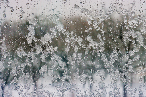 Drops of ice and rain on a window overlooking a winter snow-covered forest. Ice and water on the window close-up.