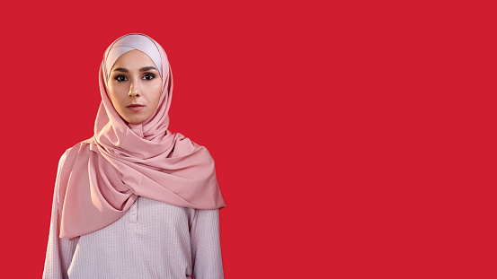 Scared face. Fear anxiety. Panic shock. Portrait of worried terrified overwhelmed woman in hijab isolated on red empty space background.