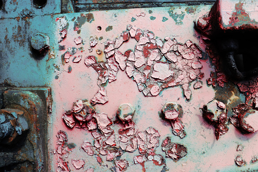 A fragment of the side of an old, abandoned steam locomotive with peeling paint and bolts.
