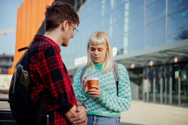 University students standing at campus and chatting on coffee break. Urban gen z college students standing near university building and chatting while having a coffee break between lectures.Copy space