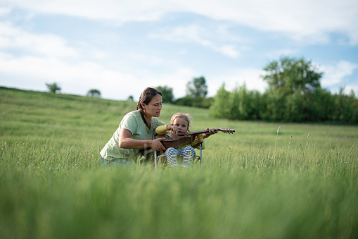 Nature Lovers. Mother and Daughter Play the Guitar in Green Meadow on a Spring Day. Teach Gen Alpha Kids to Love Nature.