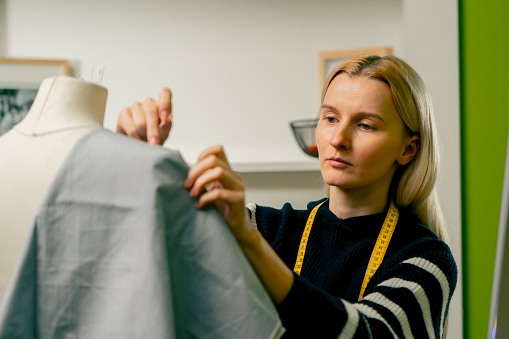 in a sewing workshop seamstress works with a mannequin and pins blue fabric with a pin