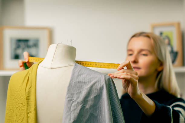 istock in a sewing workshop seamstress works with a mannequin on a blue fabric measures with a centimeter 2149750171