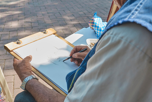 A man is drawing a picture on a piece of paper. He is using a pen and is sitting on a chair