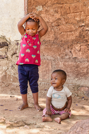 two african villager children playing outdoors in front of the house in a village,