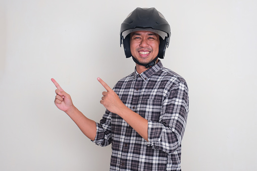 A man wearing motorcycle helmet smiling and pointing beside him