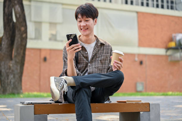 istock A happy young Asian male college student sits on a bench in the campus park using his smartphone. 2149759032