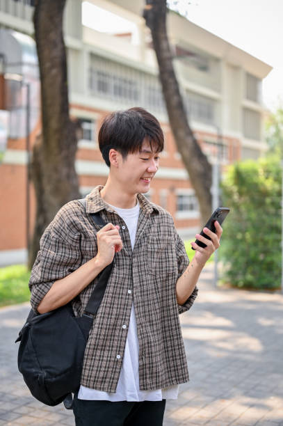 istock A happy Asian male college student is using his smartphone while walking in the campus park. 2149759044
