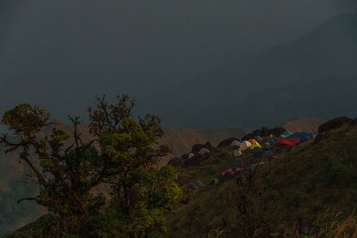 A group of tents are set up on a hillside, with a cloudy sky in the background