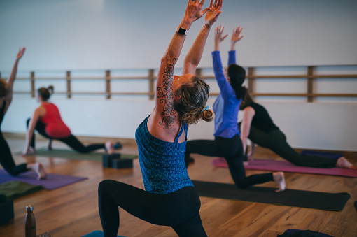 A group of strong women hold a low lunge stretch while attending a community yoga class in a clean fitness studio.