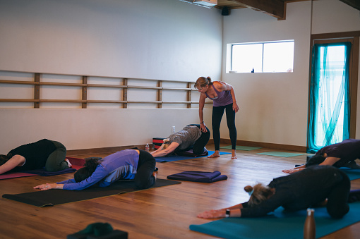 A healthy and active yoga instructor leads a restorative and relaxing yoga class in a fitness studio filled with community members.