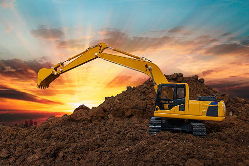Yellow Excavators are digging the soil in the construction site on the sunset sky background,With bucket lift up