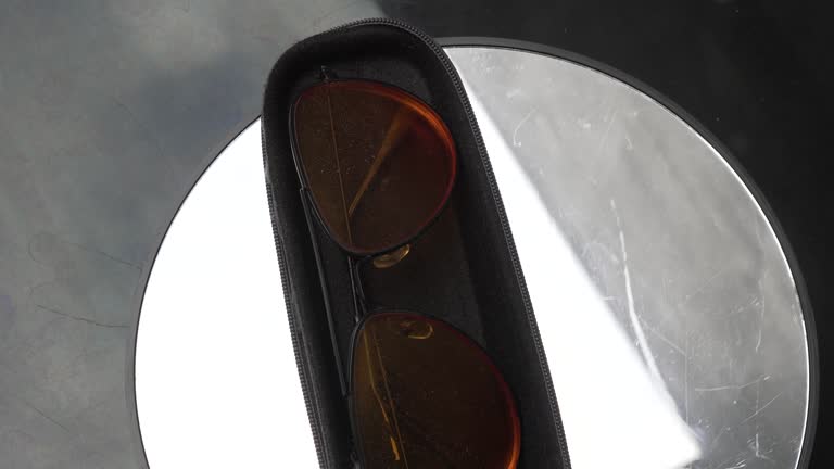 Adult men's glasses with orange lenses are placed in a black foam-padded case