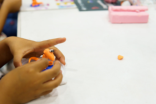 A child is playing with a toy that looks like a lizard. The toy is made of clay and is sitting on a table. The child is holding the toy with one hand and pointing at it with the other