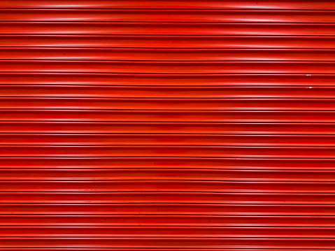 close-up of a corrugated red metal sheet, commonly used in slide doors and roller shutters. The rhythmic pattern of ridges and grooves plays with light and shadow, creating a dynamic texture that is both industrial and artistic. The glossy finish and subtle imperfections add character and depth, making it an ideal background for design projects that require a touch of vibrant energy.