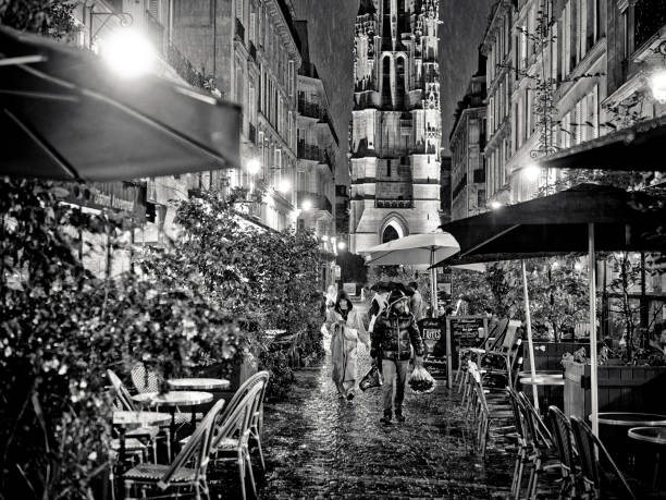 The City of Paris France on October 21, 2023:     Street vendor walking down an alley selling flowers to patrons seated at sidewalk cafes during a rainy Paris night