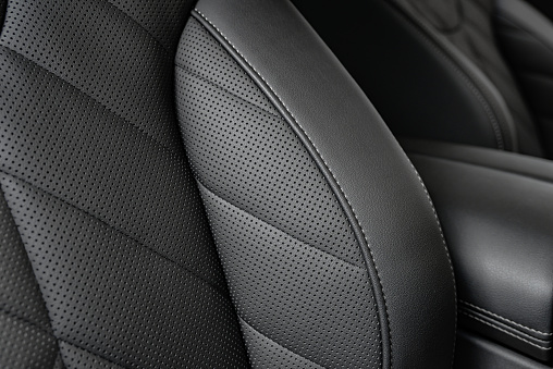 Closeup of a black perforated leather seat with stitching details in a modern sporty car.  Shallow focus.  Monochromatic.