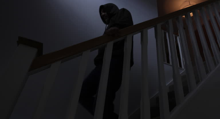 Silhouette hooded man walking downstairs at night, side view.