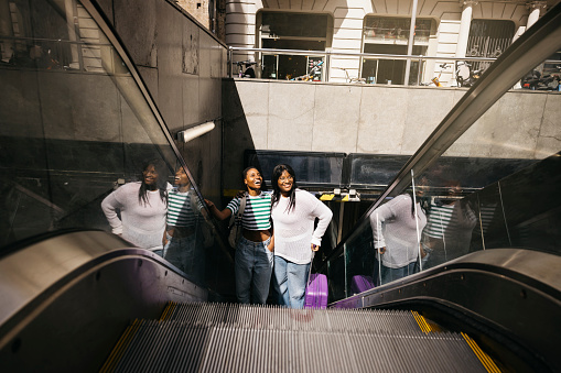 Young female couple getting off the the metro throught the escalators and reaching for the first time in a new city. Their faces reflect excitement and happiness as they begin their trip.