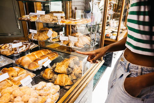 Young black woman gazing at the window display of a pastry shop and pointing with her finger the sweet she deserves.