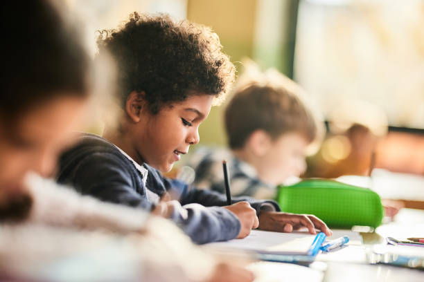 Smiling black schoolboy writing on a class at elementary school. Smiling African American elementary student writing on a class at school. elementary student stock pictures, royalty-free photos & images