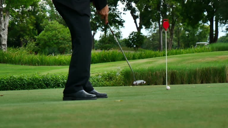 Businessman playing Golf ball practice hit swing on tee in golf club outdoor green field with recreation sport training course. Business men with black Suit driving golf Hobbies