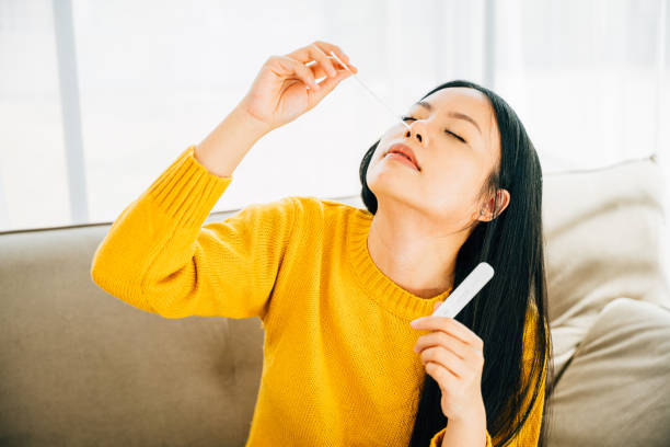 Woman at home uses a rapid antigen test kit inserting a swab into her nose