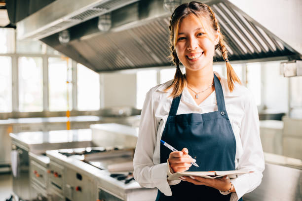 istock A young woman chef's confident portrait in commercial kitchen. Note book pen for teaching. Professional explaining expertise working with colleagues exuding confidence. Foor education 2149775009