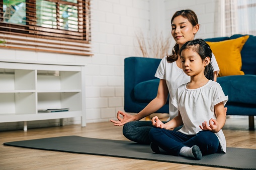 A mother teaches her daughter family yoga focusing on mindfulness and meditation in lotus position. Their smiles showcase happiness togetherness and growth.
