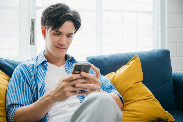 istock On a sofa at home a smiling young man talks on the phone embracing communication and technology. His happiness reflects successful living and relaxation. scrolling on social media. 2149775160