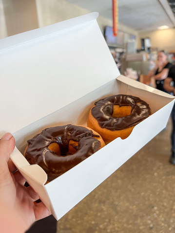 donuts, female hand holds two piece delicious chocolate donut desserts in white box in a take away fast food restaurant or cafe in America. American fast food concept. take away cafe background