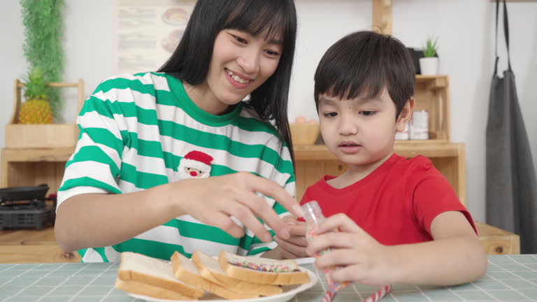 Young boy making an chocolate sandwiches at the breakfast table with his Asian mother in the kitchen