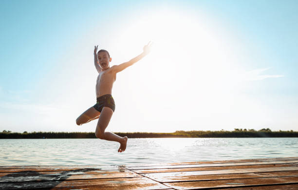 Young boy having fun enjoying a summer day jumping at the lake.