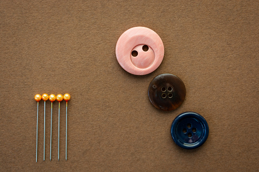 High angle view of a buttons and sewing push pins against brown background